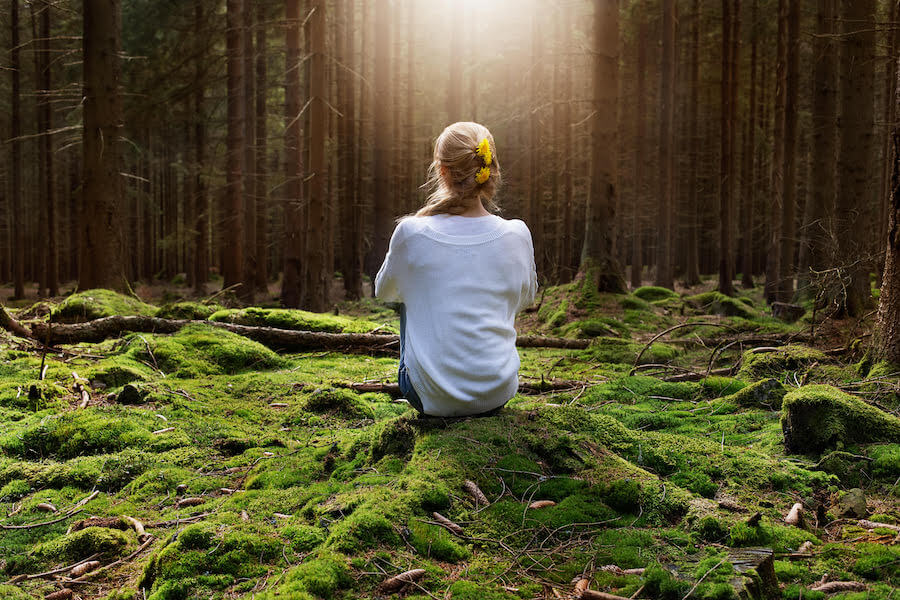 Young female sitting alone in green forest enjoys the silence and beauty of nature.