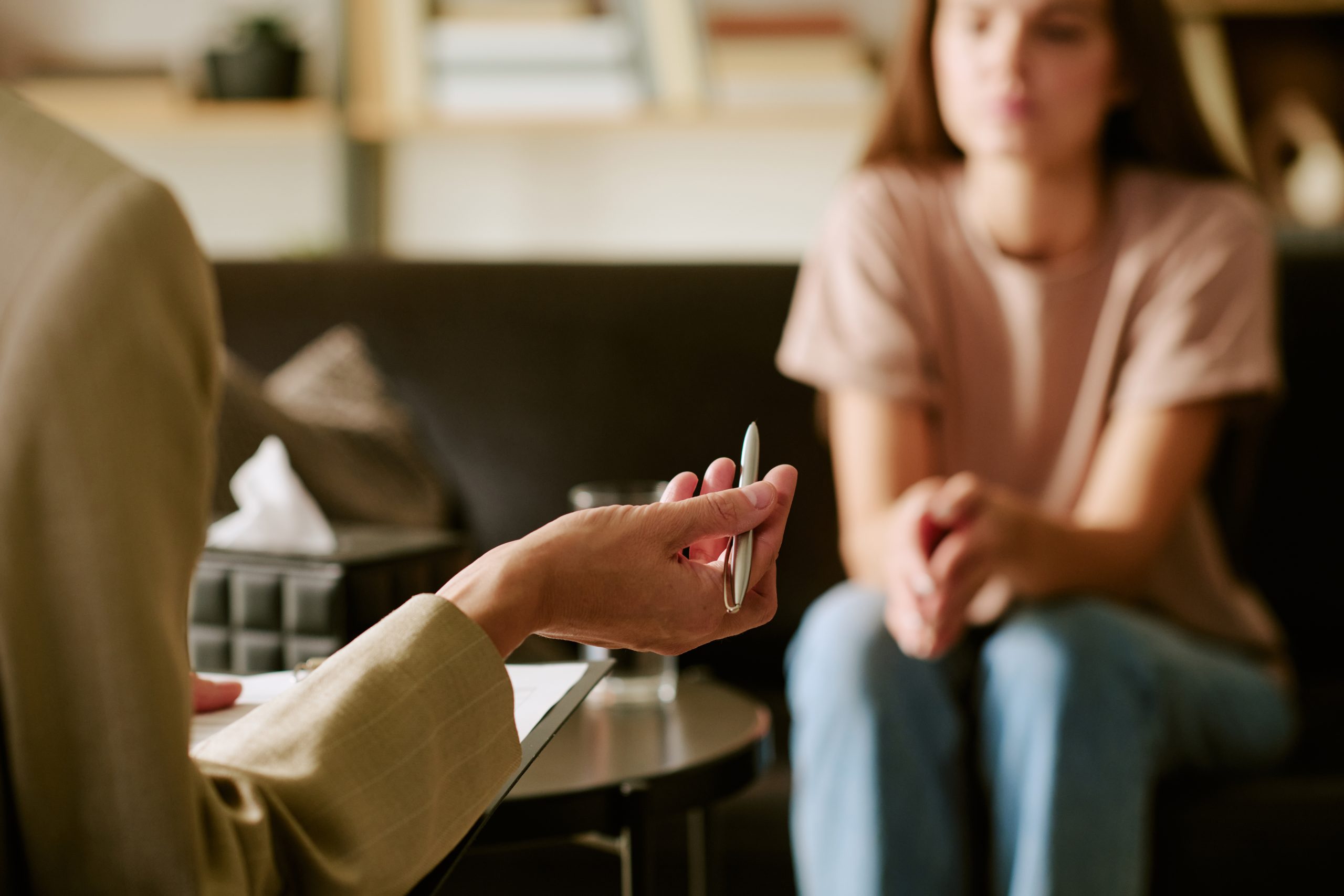 Caucasian young adult woman sitting on couch listening to middle aged Caucasian man holding pen during psychological counseling session in office setting