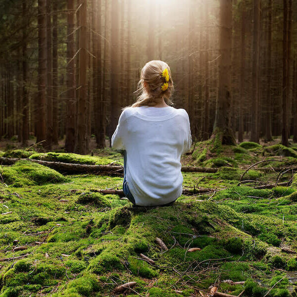 Young female sitting alone in green forest enjoys the silence and beauty of nature.