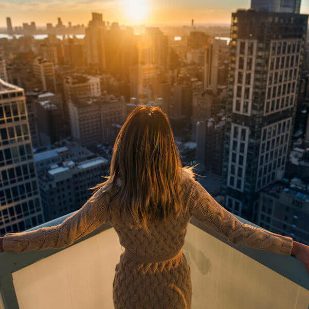 Rich woman enjoying the sunset standing on the balcony at luxury apartments in New York City.